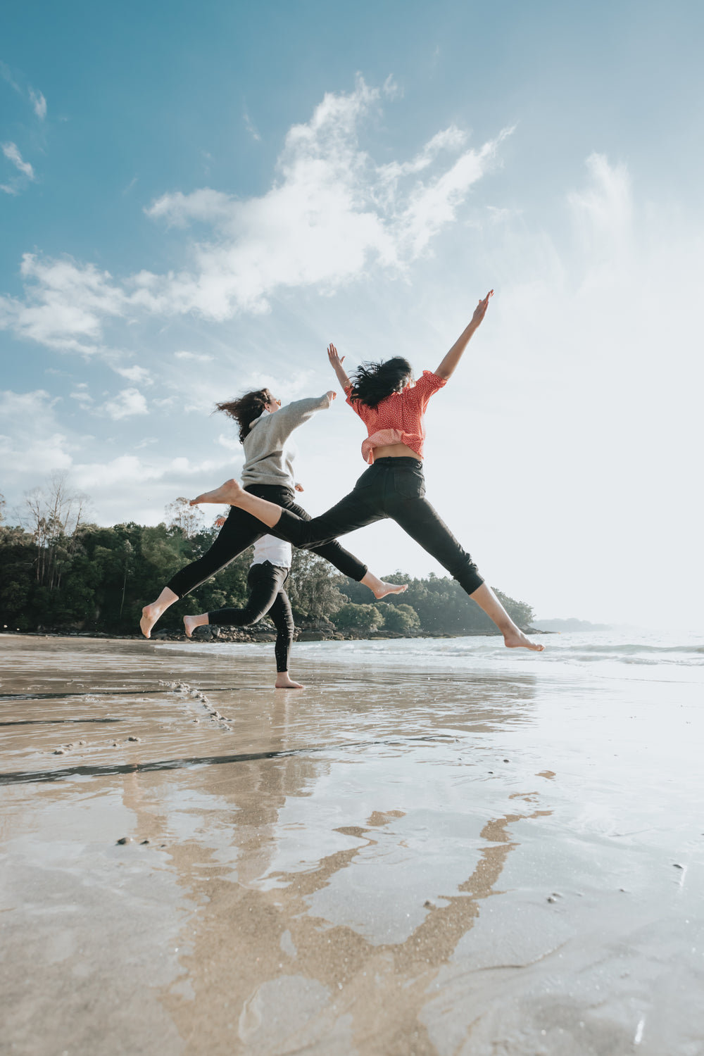 three people jump high on a wet sandy beach