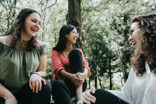 three people laughing under a tree in a forest