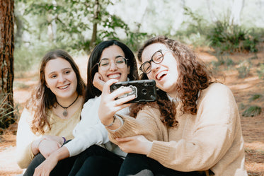 three people look at a cellphone while together outdoors