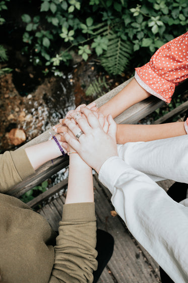 three people pile their hands up on a wooden railing