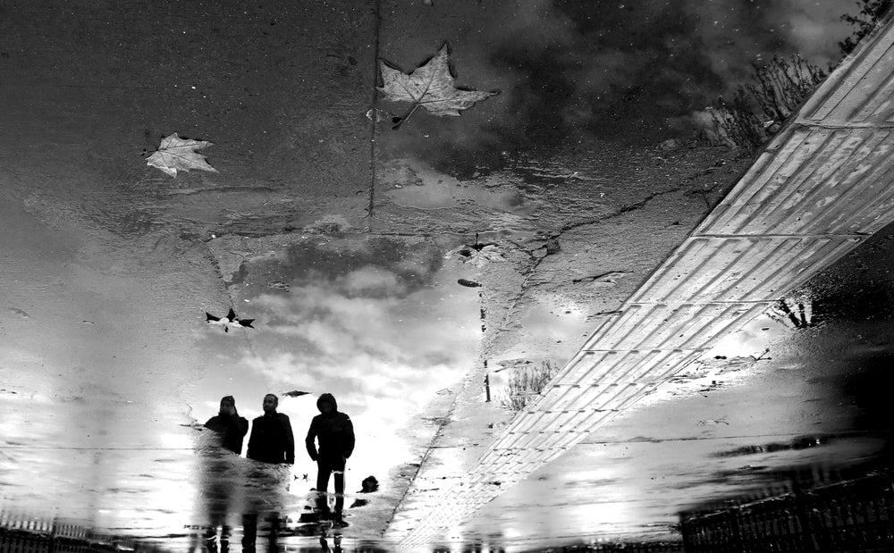 three people reflected in a puddle in black and white