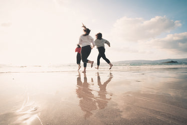 three people run towards the water on a beach