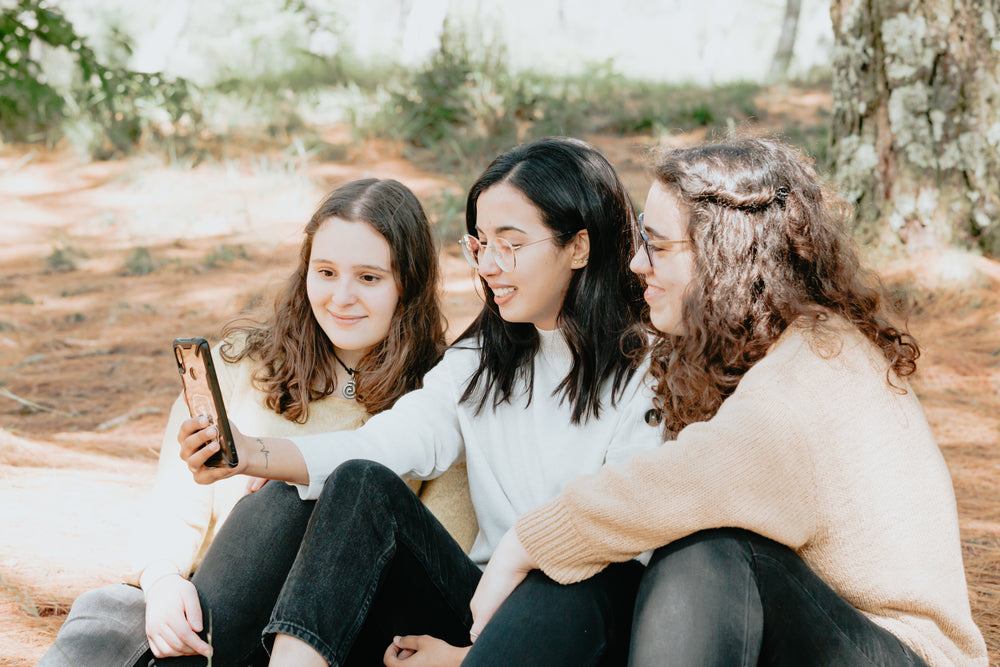 three people sit together outdoors and look at a cellphone