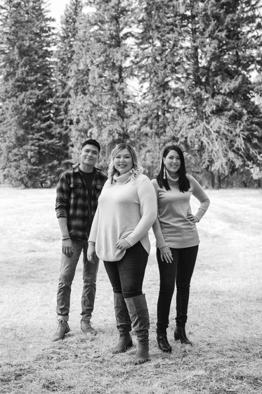 three people standing outdoors and smiling in black and white