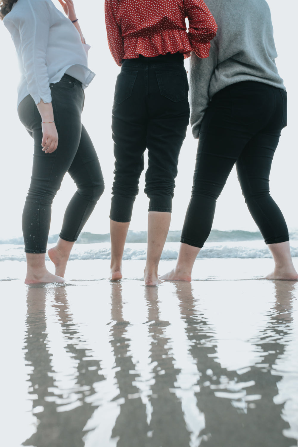 three peoples legs standing on a wet beach