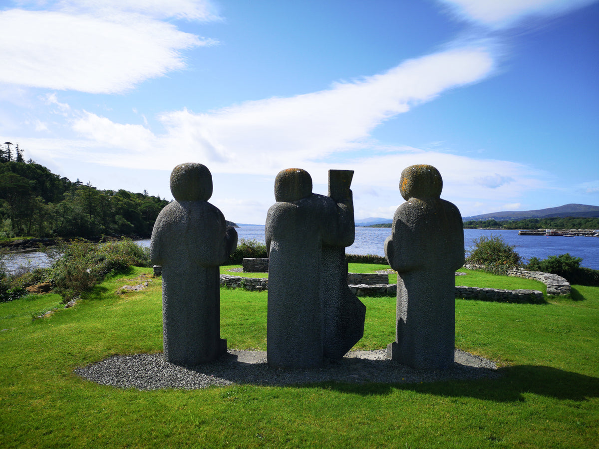 three stone figures on a grassy knoll overlook a river
