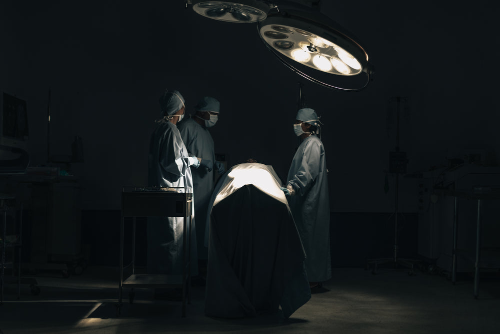 three surgeons stand around a patient