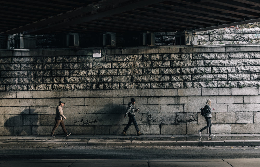 three urban pedestrians walk under bridge