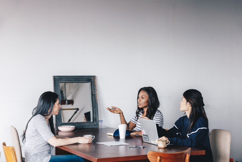 three woman hold a meeting at a dark wooden table