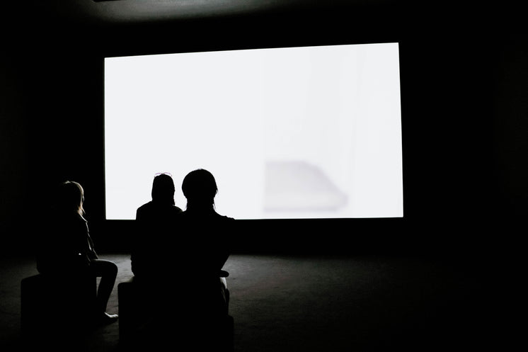 Three Woman Watch A Glowing White Screen In a Dark Room