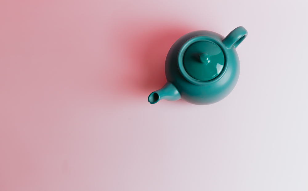 top view of a green teapot on a pink background