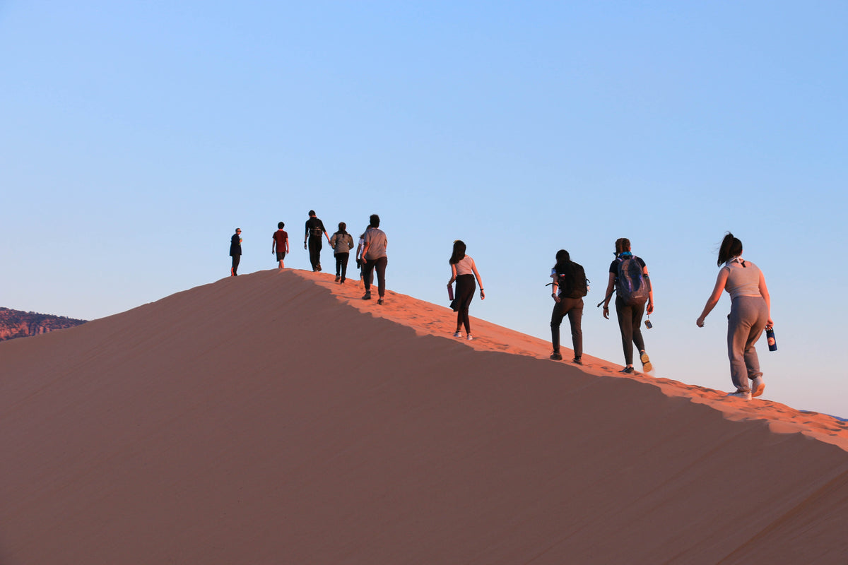 tourists hike up steep sand dune