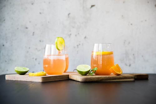 two cocktails sit on wooden boards surrounded by citrus