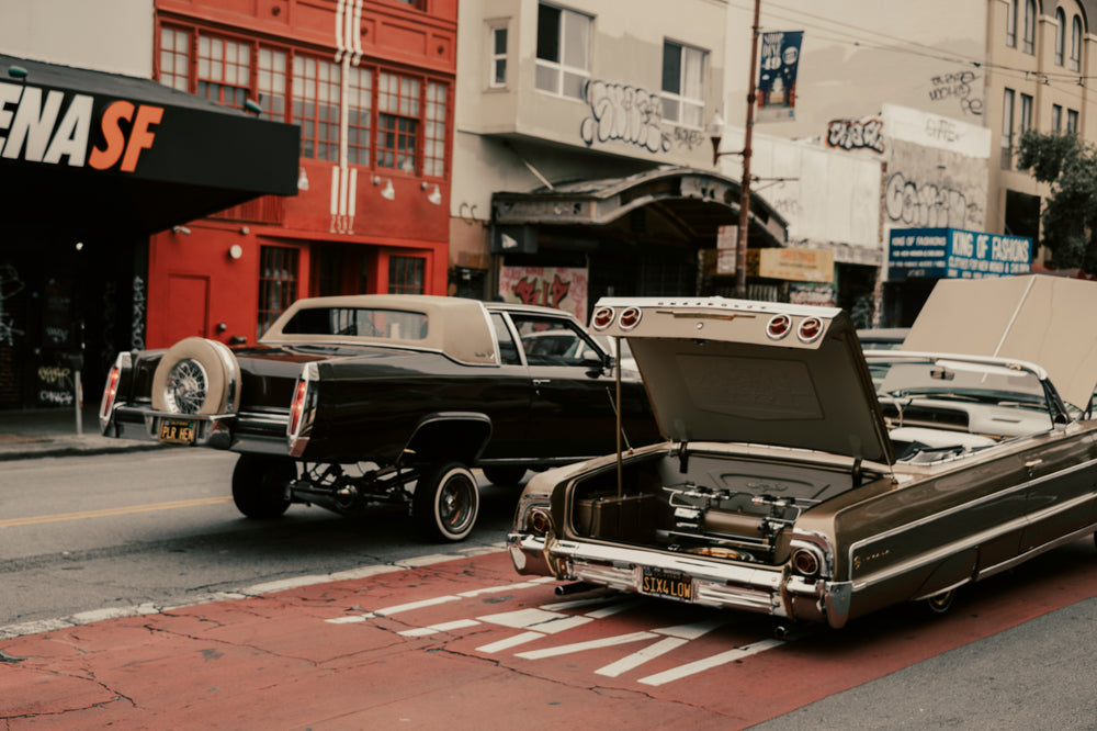  two customized cars rolling through a city street