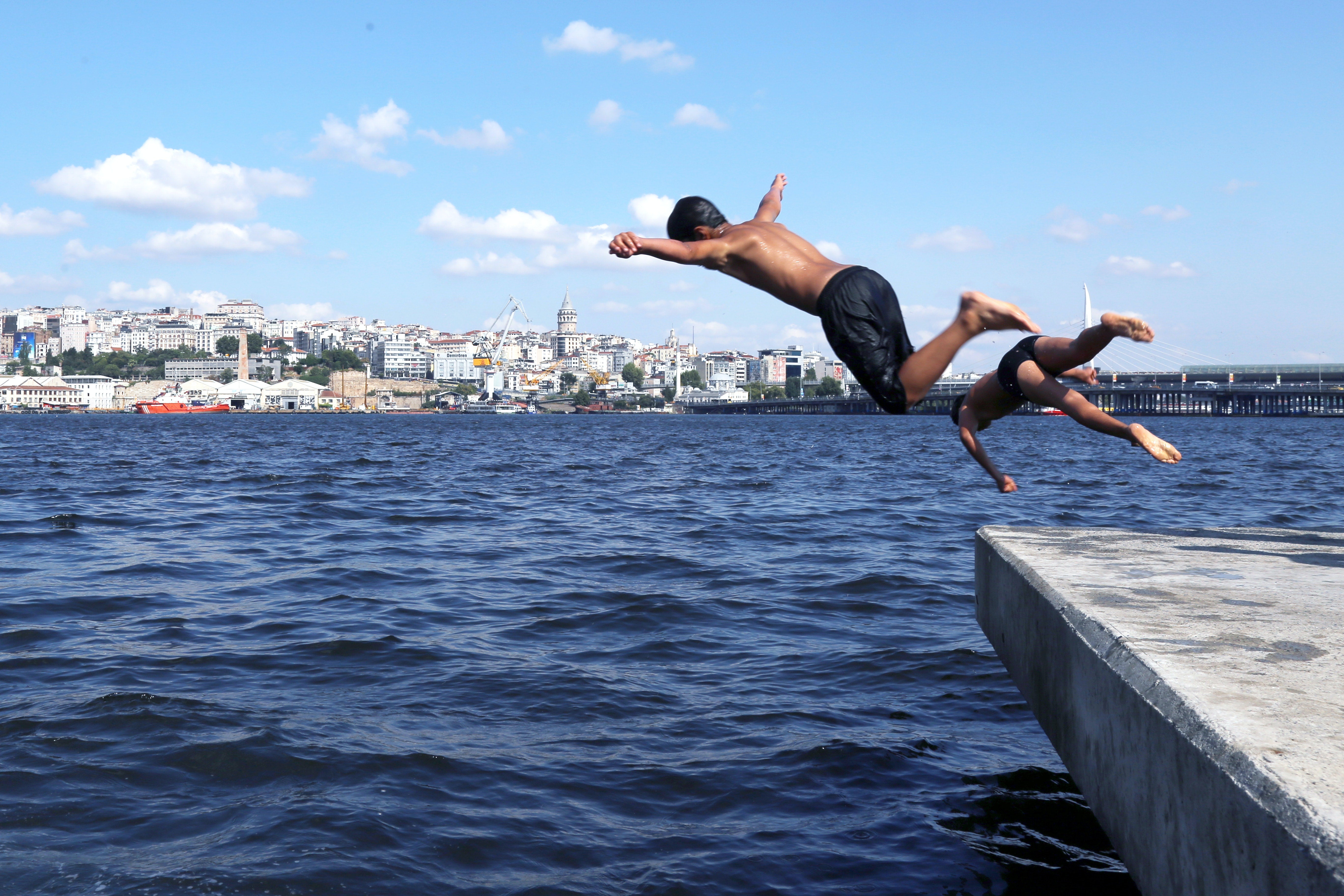 Two People Dive Into Blue Water Across From A Cityscape