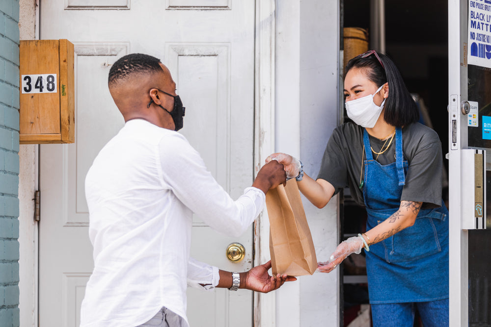 two people exchange groceries at curbside