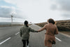 two people hold hands and walk down a paved road