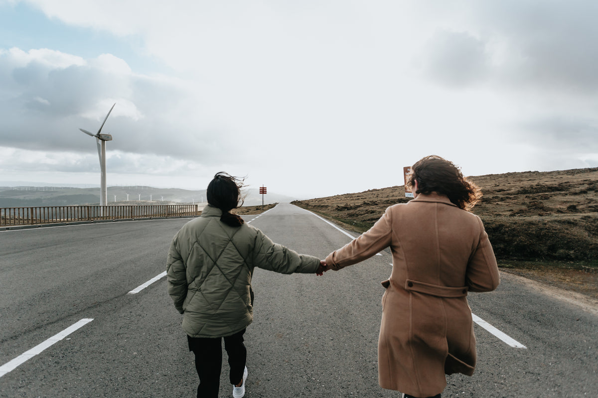 two people hold hands and walk down a paved road