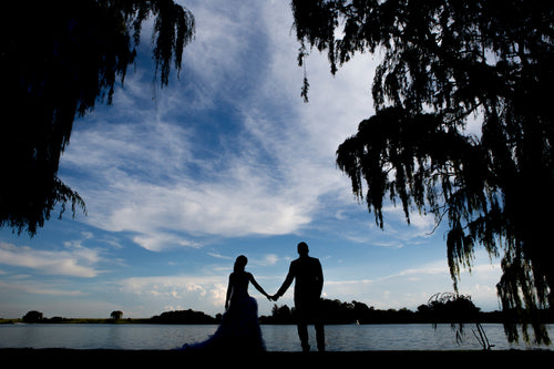 two people hold hands silhouetted against still water