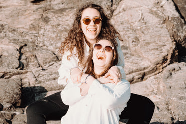 two people in sunglasses sit in front of a large brown rock