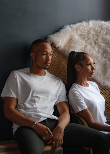 two people in tshirts sit by a black wall