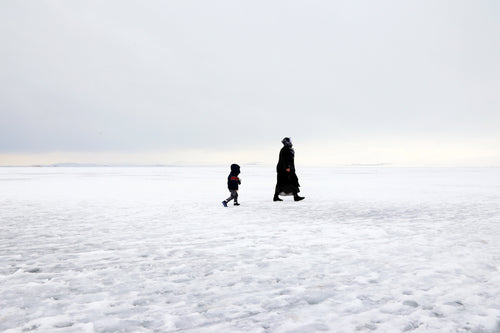 two people in winter coats walking on a field of snow