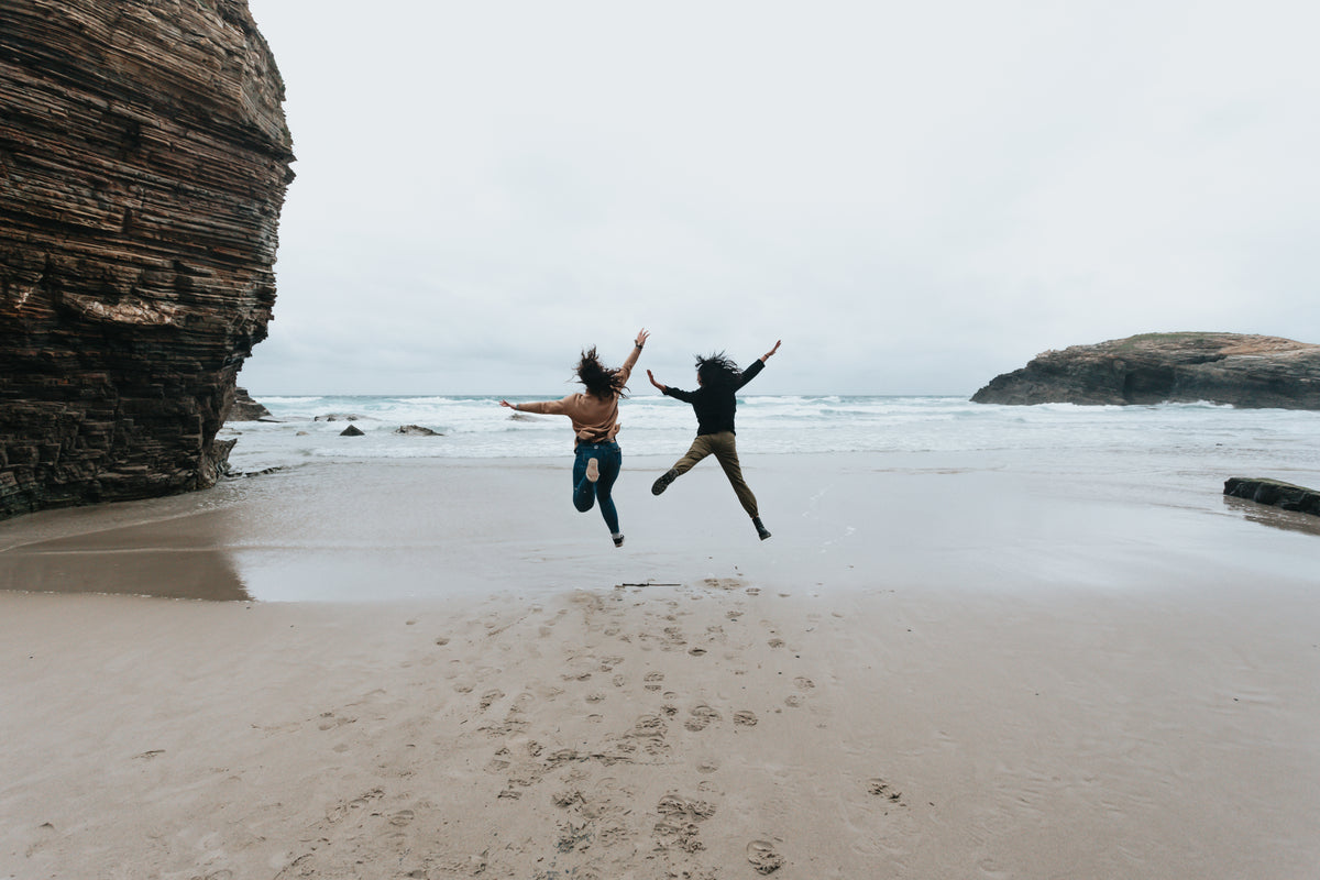 two people jump high on a sandy beach