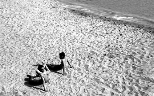 two people laying back on a sandy beach in black and white