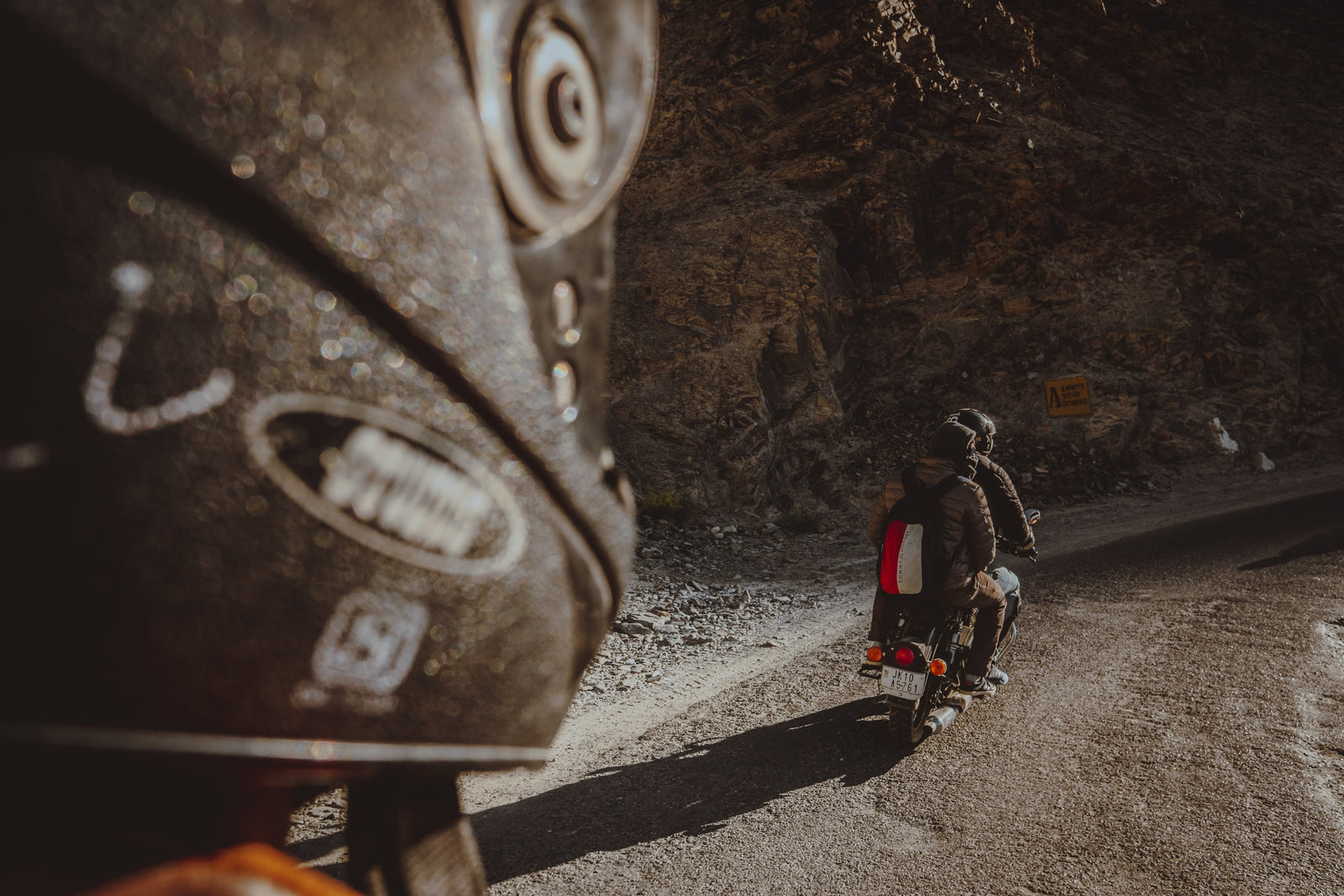 Two riders touring on a motorbike along a dirt road