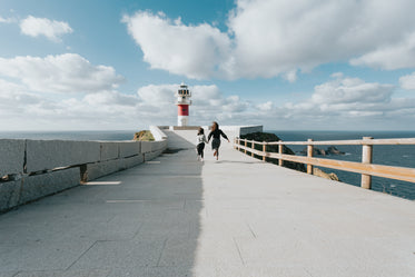 two people run down a paved road towards a lighthouse