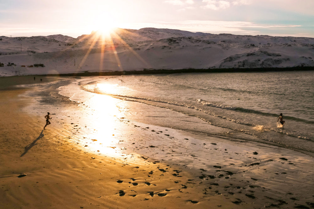 two people run into the water on a beach in winter