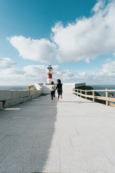 two people run towards a red and white lighthouse