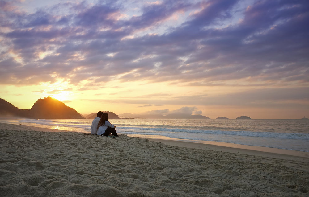 two people sit on the beach and watch the sunset