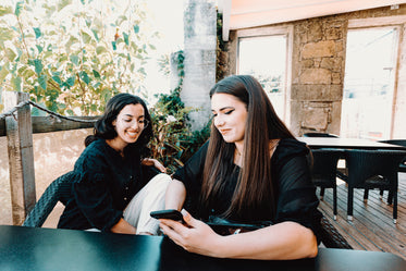 two people sits at a table and one looks at their cell phone