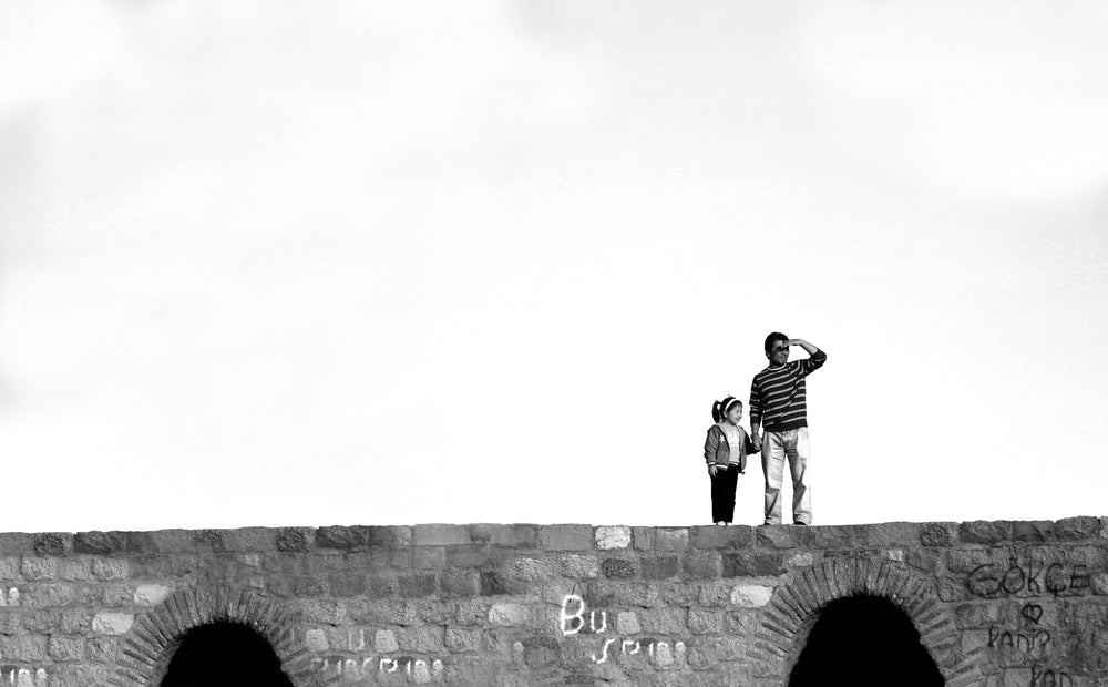 two people standing on a stone bridge in black and white