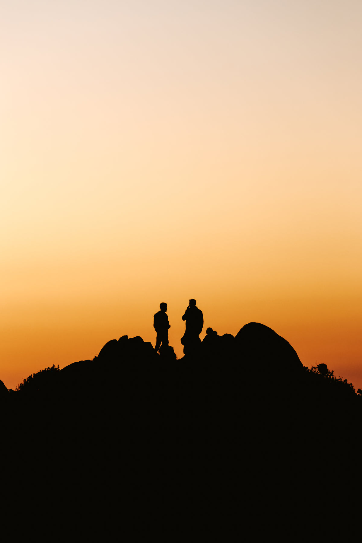 two people stands on a hill silhouetted by the sunset