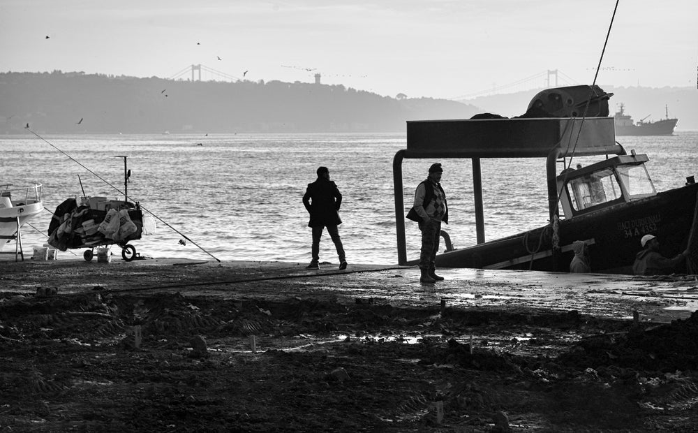 two people stands on the shore next to a boat