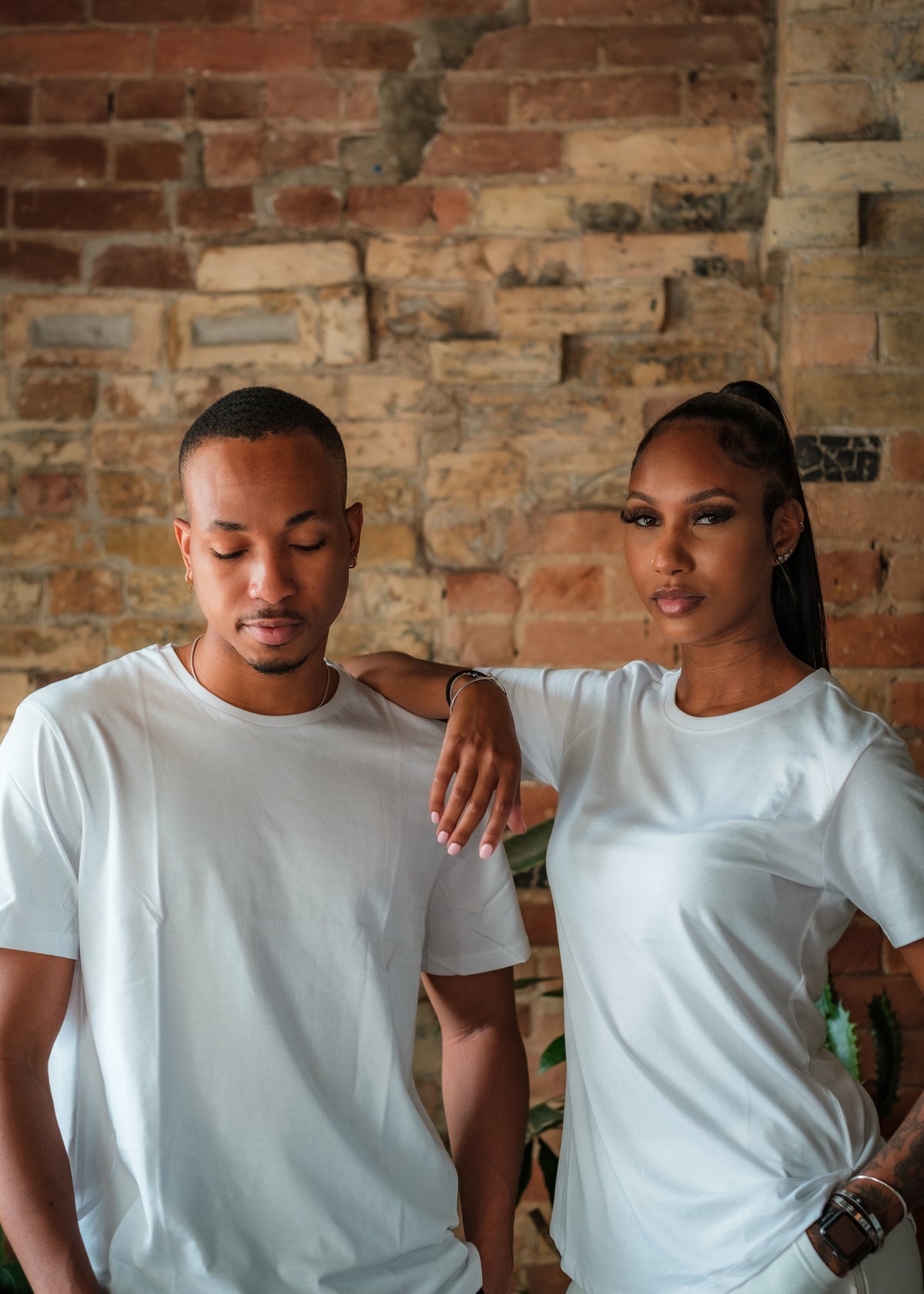 two people stands together in front of a red brick wall