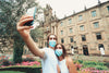 two people take a selfie outdoors while wearing blue facemasks