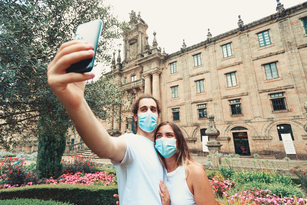two people take a selfie outdoors while wearing blue facemasks