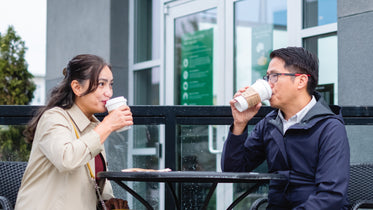 two people take sips from their coffee outside