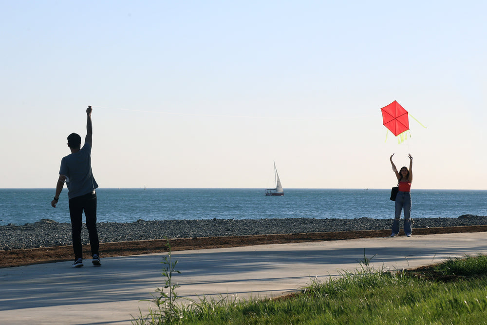 two people try and fly a red kite by the water