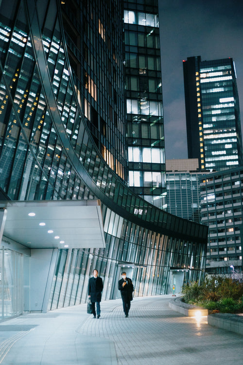 two people walk beside a tall glass building at night