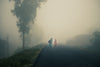 two people walk on an empty foggy road