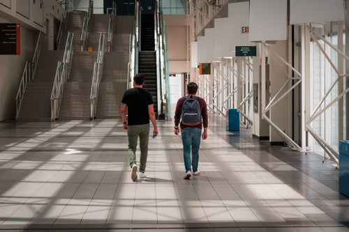two people walk towards tall stairs in an atrium