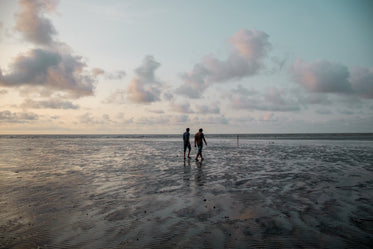 two people walking along the beach at sunset