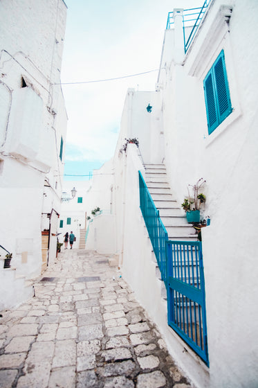 two people walking around white buildings and blue shutters