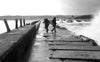 two people walking by choppy ocean tide in monochrome