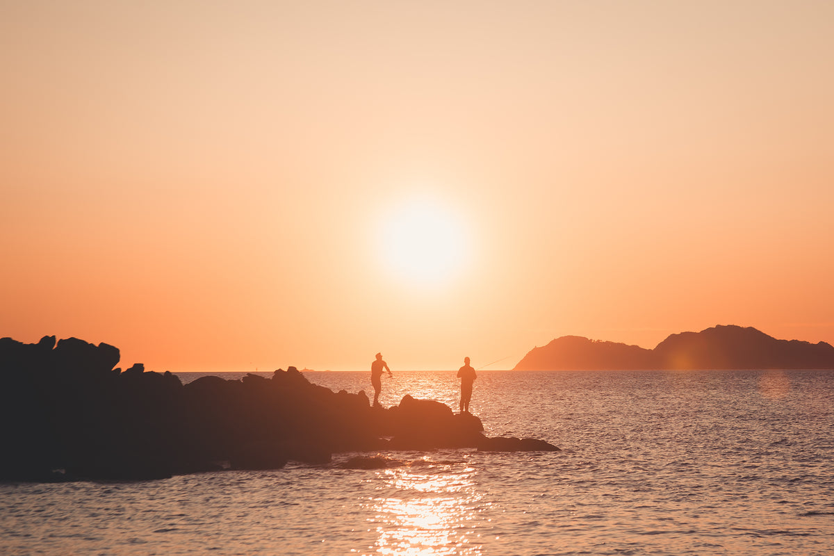 two silhouettes of people fishing at sunset