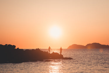 two silhouettes of people fishing at sunset